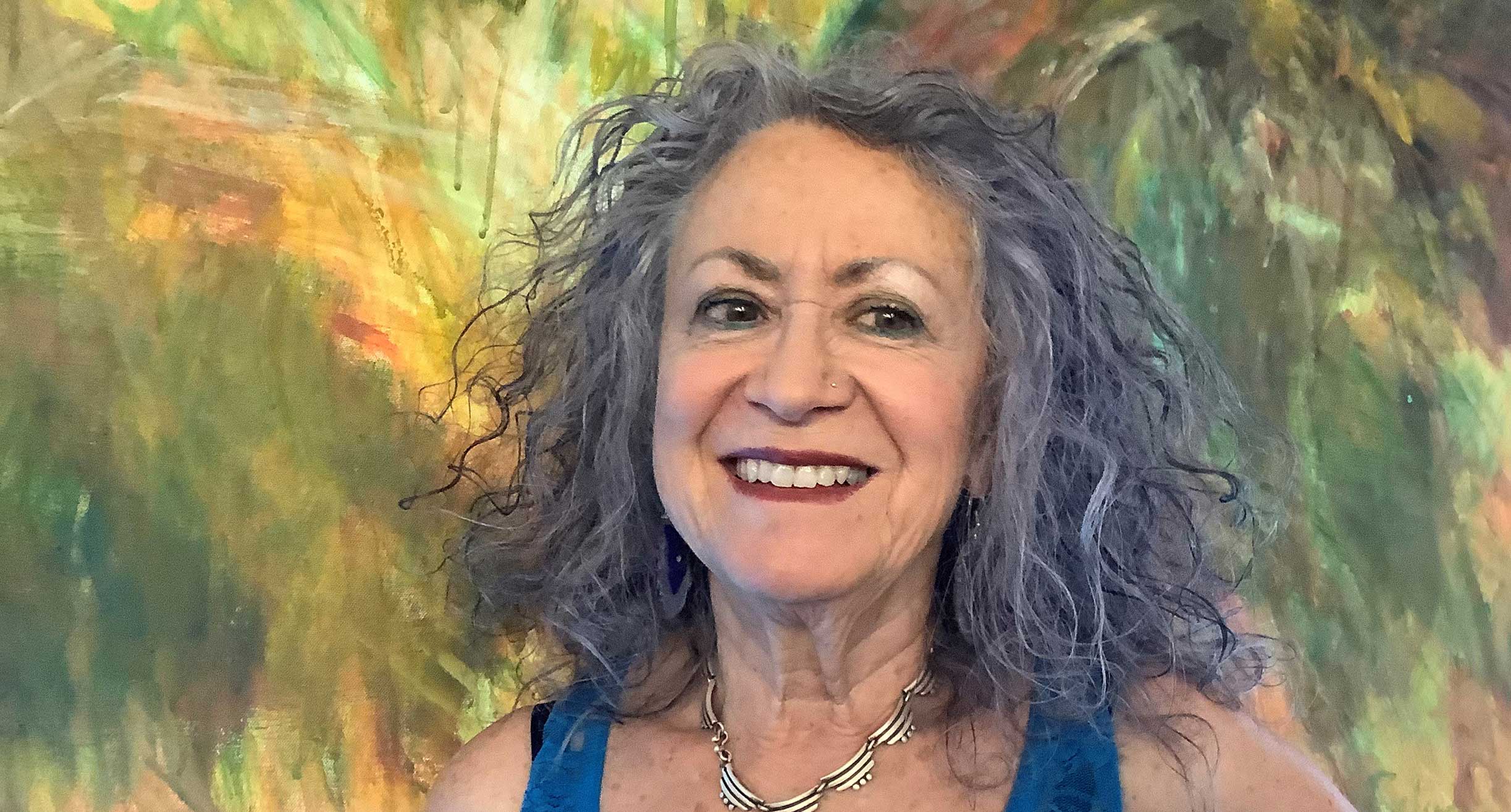 photograph of Dixie Salazar in front of her painting in greens and yellows